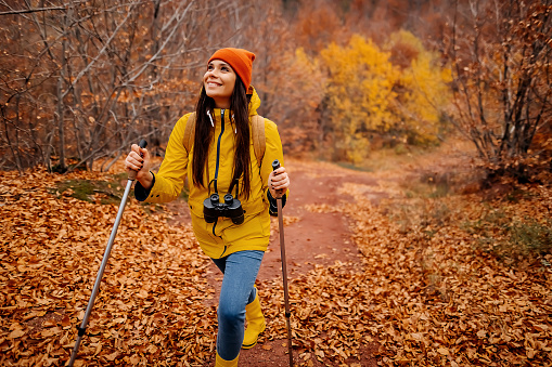 Active young woman carrying backpack hiking through the forest, enjoying beautiful autumn day outdoors