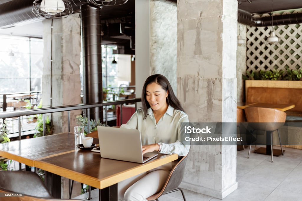 She's devoted to her career Focused Mongolian business woman sit on cafe working on laptop, concentrated serious asian female working with computer and notebook in coffee shop, freelancer, studying online, browse internet, checking bills 25-29 Years Stock Photo