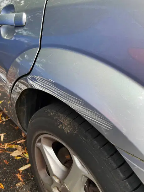 stock photo showing a silver metallic car wheel arch that has been freshly scratched after a parking accident caused by another driver in a supermarket car park. This photo concept shows primer and colour coat scratches in need of respraying at a garage, and maybe a car insurance claim.