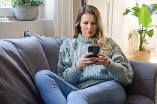 istock attractive middle aged woman sitting on the couch (negative emotions, smartphone)) 1351720238