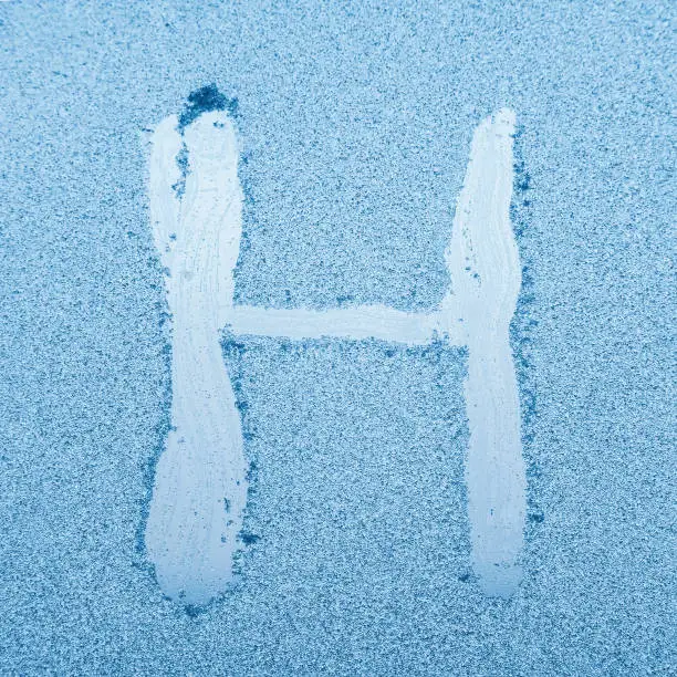 The letter H written on glass with frost in the frost in winter, close up.