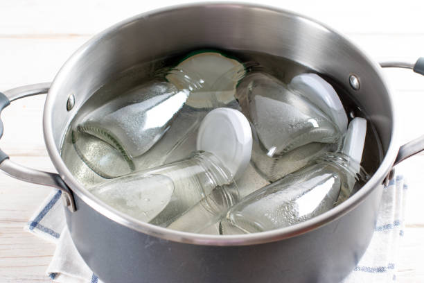 Sterilizing glass jars in a steel pan. Steaming bubbling wather Sterilizing glass jars in a steel pan; steaming bubbling wather boiled water stock pictures, royalty-free photos & images