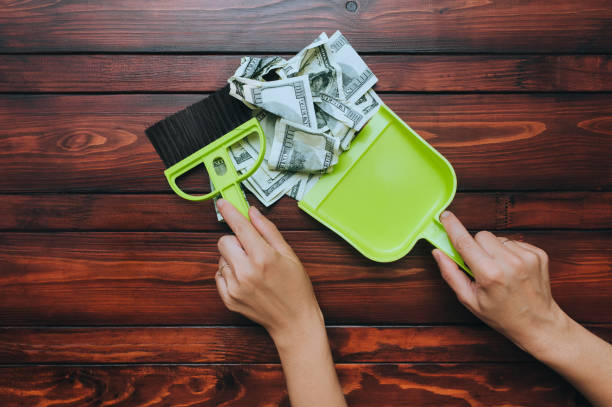 Two female hands hold a brush and scoop and remove dollar bills from the wooden table. The concept of devaluation, depreciation, inflation and default, when money loses its value. stock photo