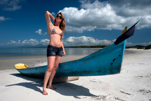 Young woman poses next to a boat on the beach of Ilha do Mel (Honey Island) on the south coast of Brazil