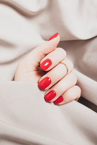 Female hand with bright red manicure on a background of beige fabric