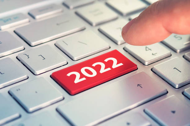istock Keyboard with text HAPPY 2022 and finger pushing the enter button. Color button on the gray silver keyboard of modern ultrabook. caption on the button 1351744912