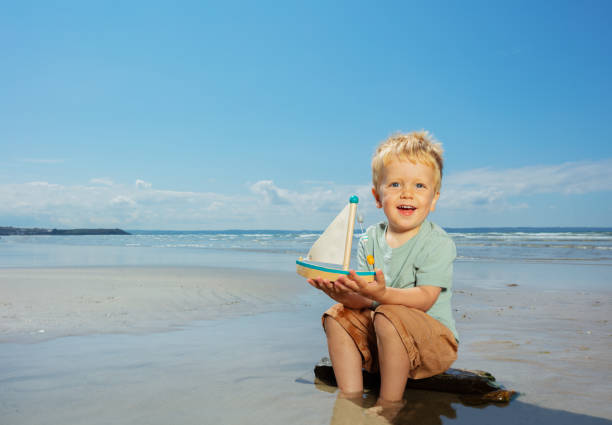 istock Boy play with toy sail ship sitting on the beach 1351745198