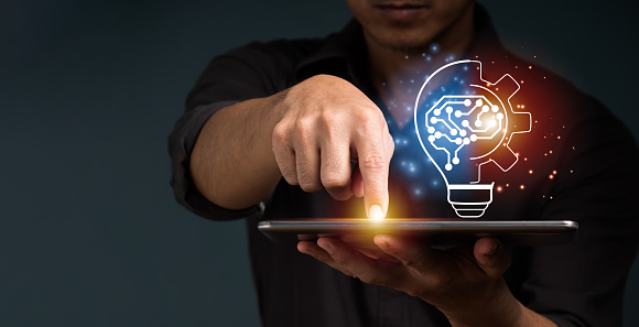 A businessman shows a concept by holding half of a virtual lightbulb and his brain on a digital tablet. Insightful concept and inspiration for creativity.