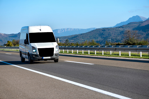 White modern delivery small shipment cargo courier van moving fast on motorway road to city urban suburb. Distribution and logistics express service. Mini bus driving on highway day. banner.