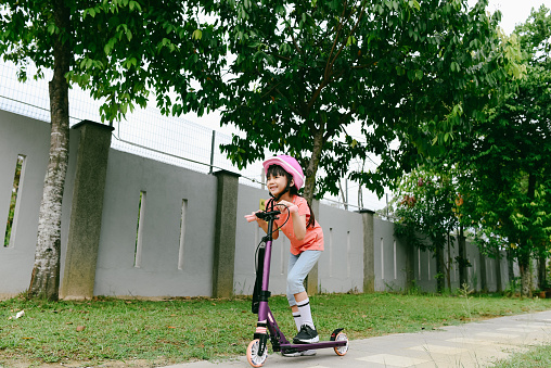Happy Asian  girl standing on push scooter at public park.