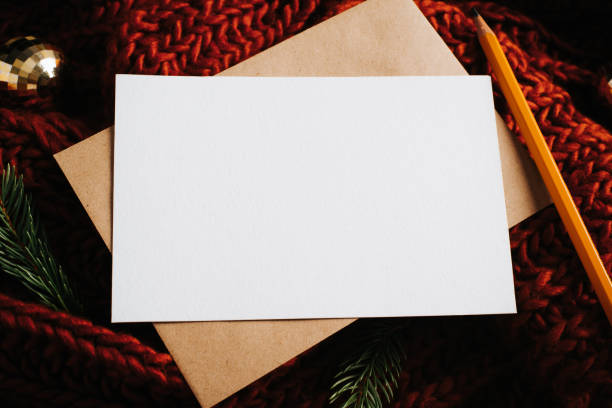 istock Christmas festive composition layout. Close-up greeting card mock-up with empty space, craft envelope, pencil, golden toy balls and sprig of pine on knittes red background. Xmas still life top view 1351788662