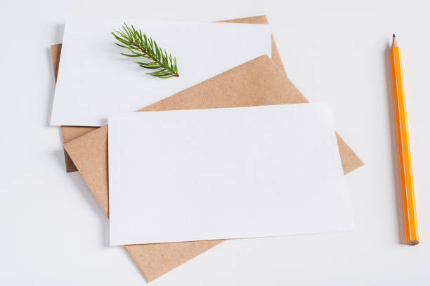 istock Xmas festive composition layout. Close-up greeting cards mock-up with blank space, craft envelope, pencil and pine twig on white table. Merry Christmas and Happy New Year concept 1351788663