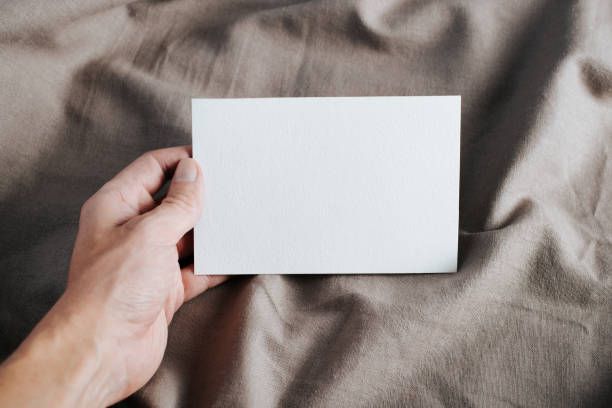 istock Close-up of hand holding white greeting card mock-up with empty space on rustic textile background 1351788677