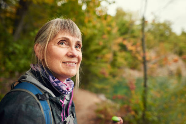 Smiling senior woman enjoying an autumn hike in a forest Senior woman wearing outdoor gear smiling and admiring the autumn scenery while out for a hike in a forest 60 69 years stock pictures, royalty-free photos & images
