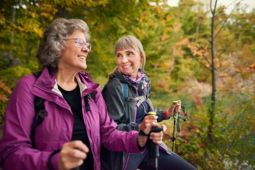 Two senior women in outdoor gear laughing while out for a hike together in a forest in the autumn
