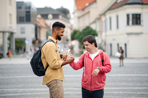 A young man with Down syndrome and his mentoring friend meeting and greeting outdoors in town