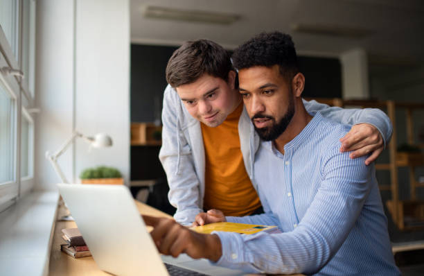 istock Happy young man with Down syndrome and his tutor using lapotp indoors at school. 1351794266