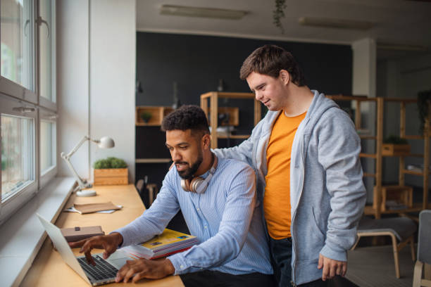 istock Happy young man with Down syndrome and his tutor using lapotp indoors at school. 1351794419
