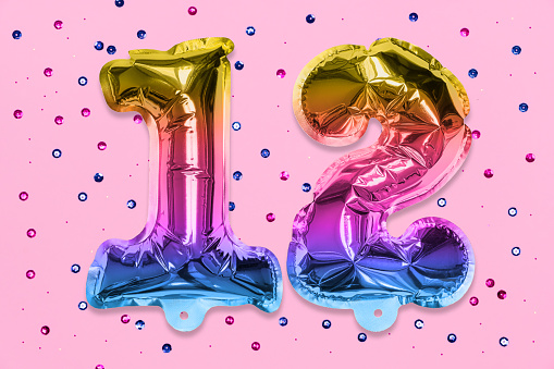 Rainbow foil balloon number, digit twelve on a pink background with sequins. Birthday greeting card with inscription 12