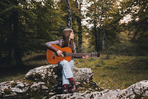Portrait of a beautiful little girl playing a Spanish guitar in the forest.