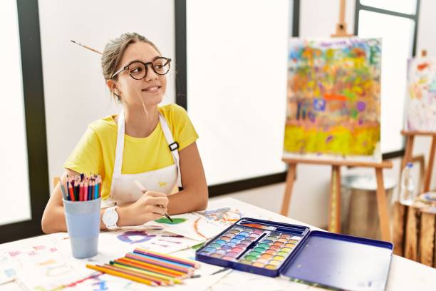 jeune adolescente brune au studio d’art regardant ailleurs avec le sourire sur le visage, l’expression naturelle. rire confiant. - artist child artists canvas indoors photos et images de collection