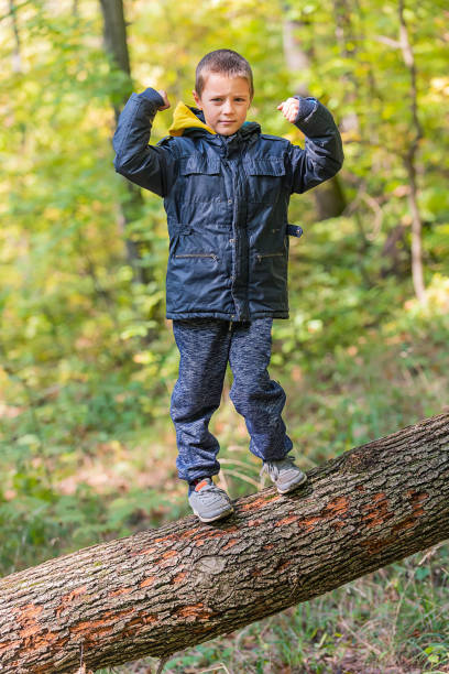 istock Young Boy standing on Fallen Down Tree Trunk and Catching Balance 1351808282