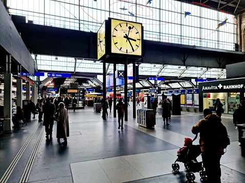Zurich Main Railway Station with people standing and walking arround. The Railway station is serving up to 2,915 trains per day, Zürich HB is one of the busiest railway stations in the world. The image was captured during winter season.