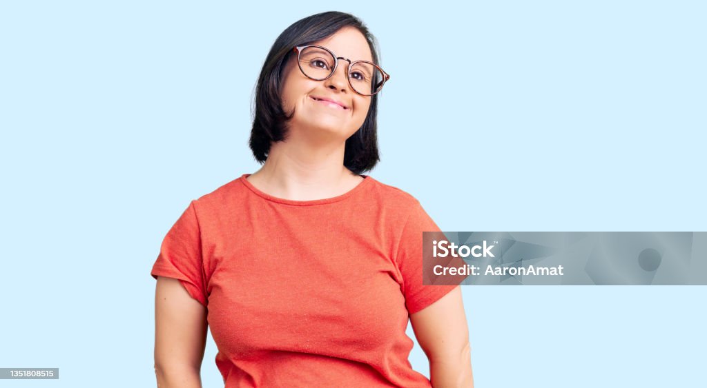 Brunette woman with down syndrome wearing casual clothes and glasses looking positive and happy standing and smiling with a confident smile showing teeth Down Syndrome Stock Photo