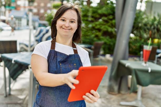 young down syndrome woman wearing apron using touchpad at coffee shop terrace - downs syndrome work bildbanksfoton och bilder