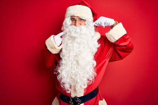 Middle age handsome man wearing Santa costume standing over isolated red background smiling cheerful showing and pointing with fingers teeth and mouth. Dental health concept.