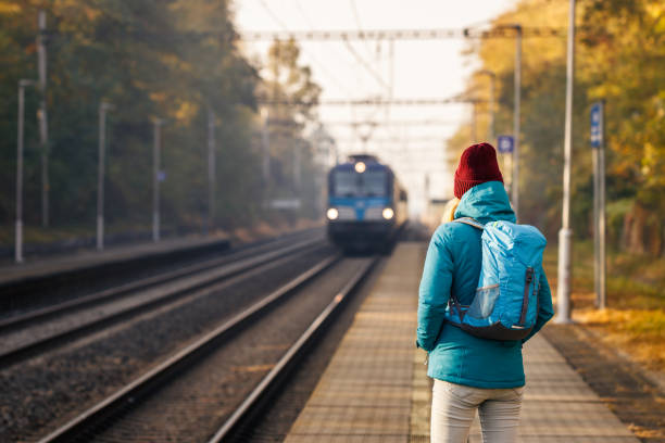 alleinreisender mit rucksack schaut auf ankommenden zug an einem bahnhof - leaving loneliness women railroad track stock-fotos und bilder