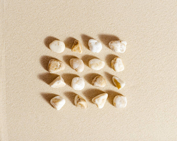 istock Pattern with white pebble sea stones on fine sand. Square composition from natural stone neutral beige color, monochrome tones. Spa minimal background 1351812970