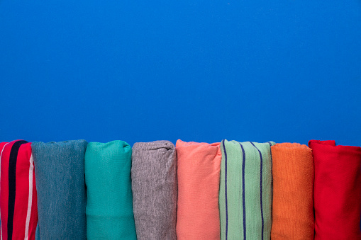 close up of rolled colorful t shirt clothes on blue table background