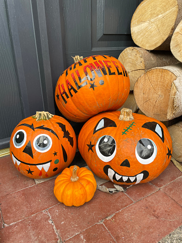 Stock photo showing a carved pumpkin head on the night of Halloween - All Hallow's Eve. Sticker faces and messages have been stuck onto pumpkins, ready to be left outside of the front door at night, to scare away the witches, spooks, ghosts and ghouls. A pumpkin by the front door also indicates that the house is happy to accept Trick or Treaters / children dressed up for a night of Trick or Treat / Treating.