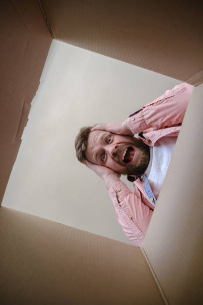 Shocked Caucasian man found the wrong order in an unpacked delivered box, he screams and grabs head with his own hands. Unboxing inside view.