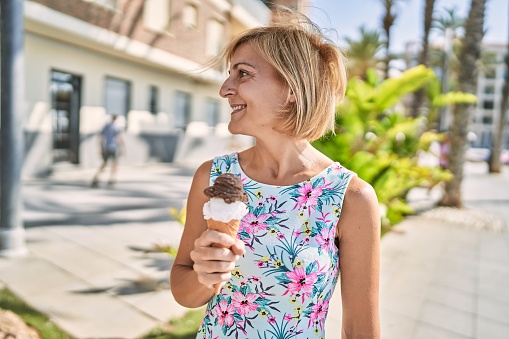 Middle age beautiful woman holding ice cream at park