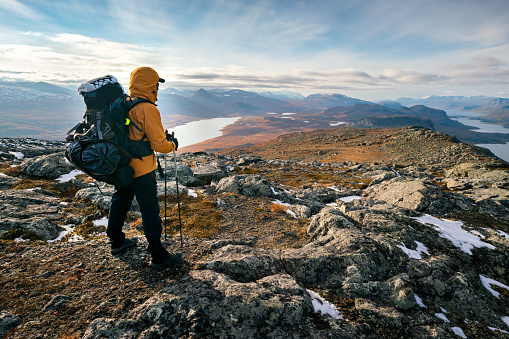 Male hiker overlooking epic view of vast arctic landscape of Stora Sjofallet National Park, Sweden, on autumn day. Mountains and valleys of Lapland. Ahkka massif. View from the top of Lulep Gierkav