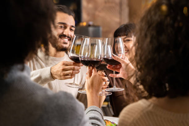 amigos brindando por el vino tinto - jóvenes tintineando sentados en la mesa del restaurante - clunking fotografías e imágenes de stock
