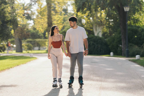 istock Young couple holding hands while skating in a path of a park 1351826988