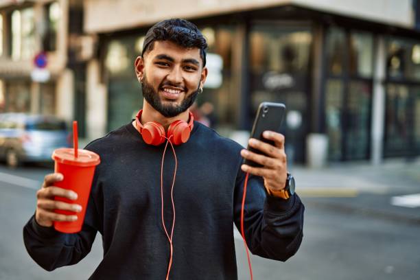 jovem árabe usando smartphone bebendo café na rua - arab style audio - fotografias e filmes do acervo