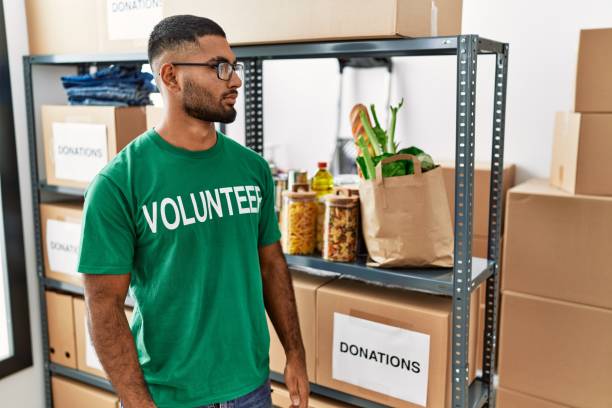 istock Young indian man volunteer holding donations box looking to side, relax profile pose with natural face with confident smile. 1351827158