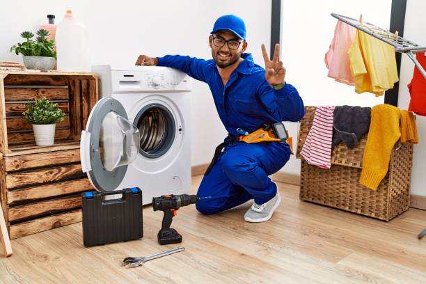istock Young indian technician working on washing machine smiling with happy face winking at the camera doing victory sign with fingers. number two. 1351827164