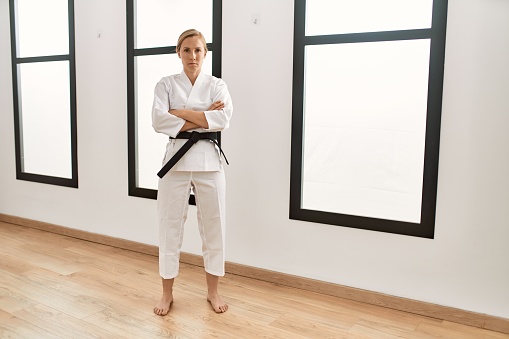 Caucasian young blonde woman wearing karate kimono and black belt skeptic and nervous, disapproving expression on face with crossed arms. negative person.