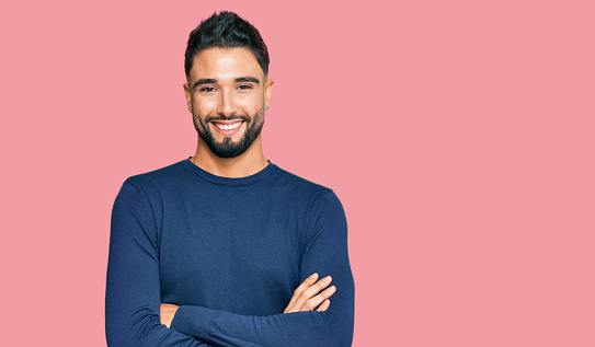 Young man with beard wearing casual blue winter sweater happy face smiling with crossed arms looking at the camera. positive person.