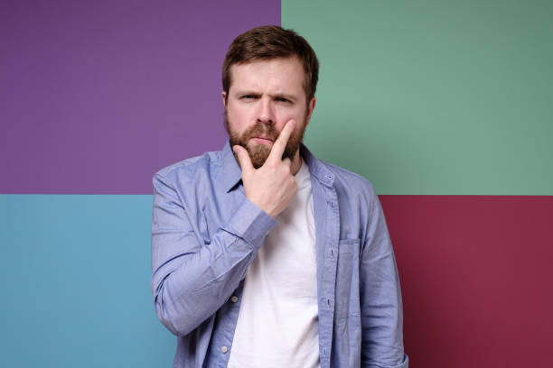 istock Pensive attractive bearded man with a suspicious look holds hand on face. 1351830987