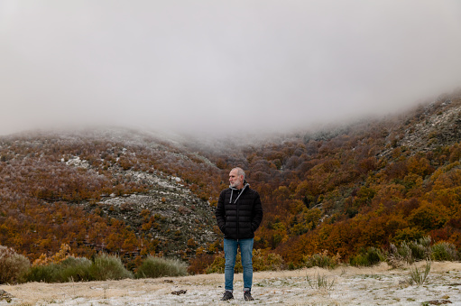 Portrait of adult man in black winter jacket against autumn color trees on mountain, in Tejera Negra, Cantalojas, Guadalajara, Spain