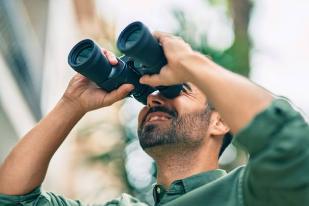 istock Young hispanic man smiling happy looking for new opportunity using binoculars at the city. 1351835006