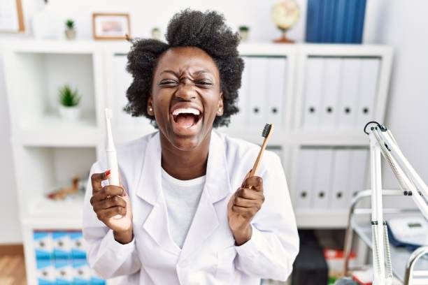 African dentist woman holding electric toothbrush and normal toothbrush smiling and laughing hard out loud because funny crazy joke. African dentist woman holding electric toothbrush and normal toothbrush smiling and laughing hard out loud because funny crazy joke. people laughing hard stock pictures, royalty-free photos & images