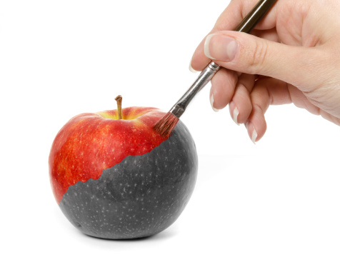 Female hand painting a fresh red apple which is partly black and white and partly colored, isolated on white background