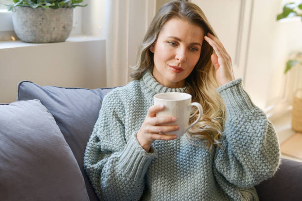istock attractive middle aged woman sitting on the couch (drinking hot tea) 1351839456